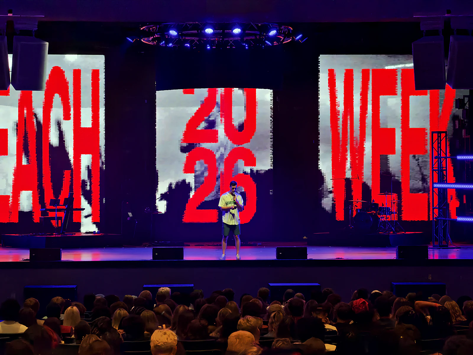 A single speaker at center stage under giant Beach Week typography, the crowd listening