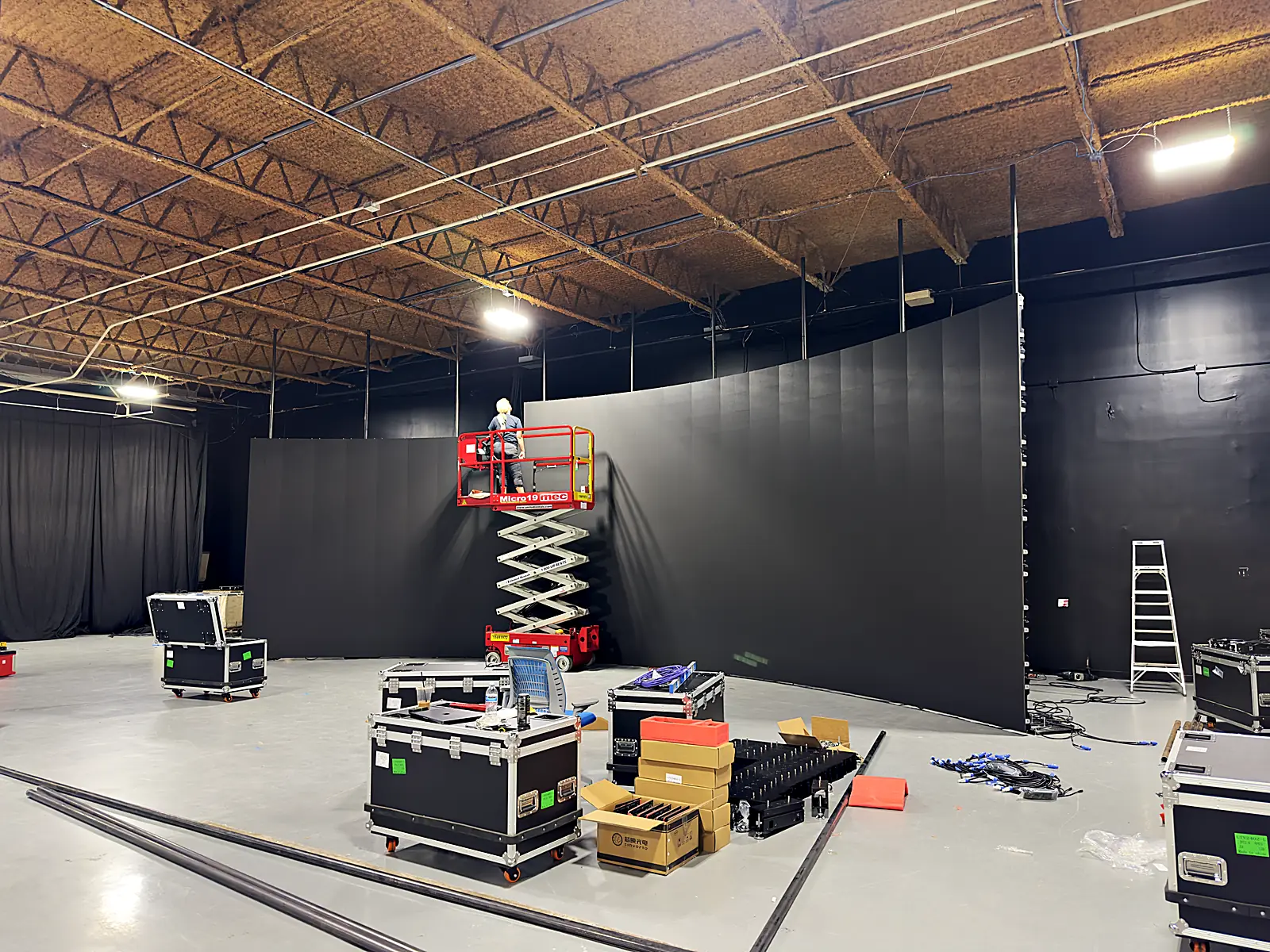 The curved LED volume mid-build: scissor lift at the wall, staged road cases across the studio floor