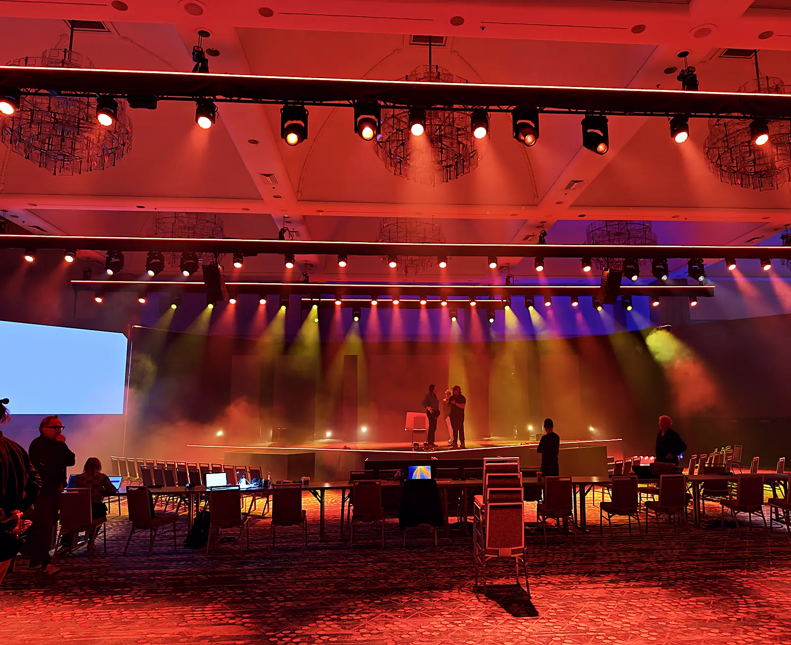 Amber rehearsal lighting over a general-session stage build in a hotel ballroom