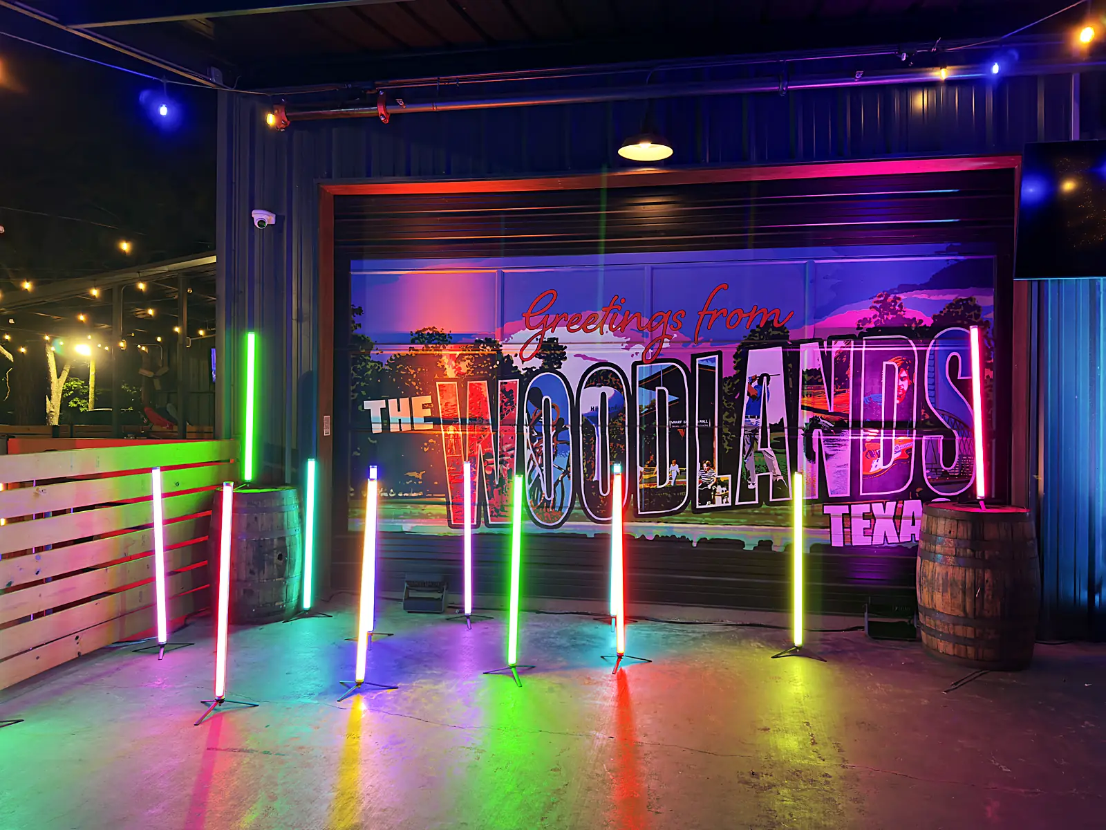 Neon Cowboy offsite: giant Greetings from The Woodlands Texas postcard backdrop with rainbow LED light tubes and whiskey barrels