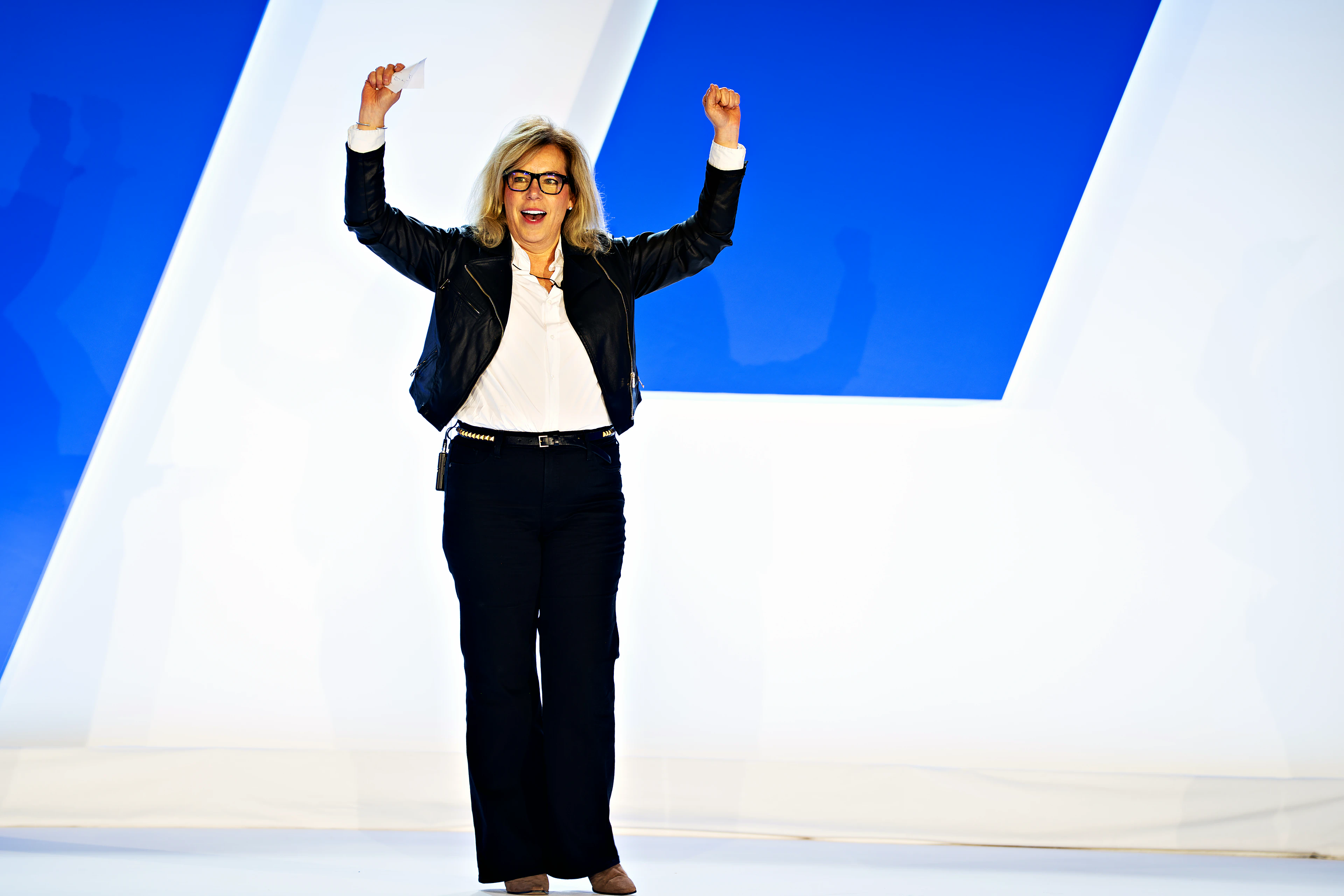 Show state: a presenter on the custom half-circle white stage, arms raised, with the One EO scenic and LED wall behind