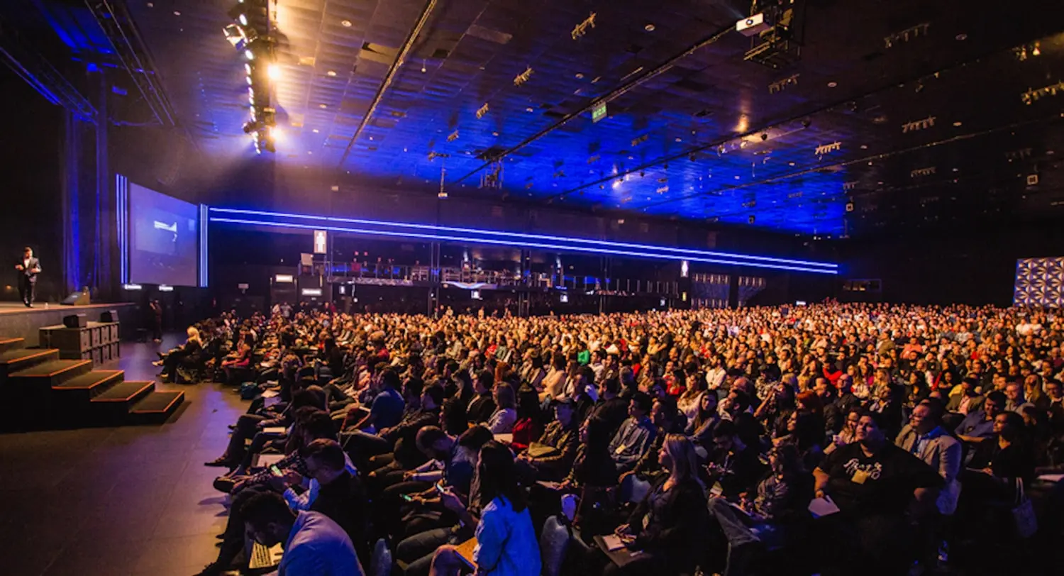 Packed general session during a hybrid keynote broadcast in a convention ballroom.