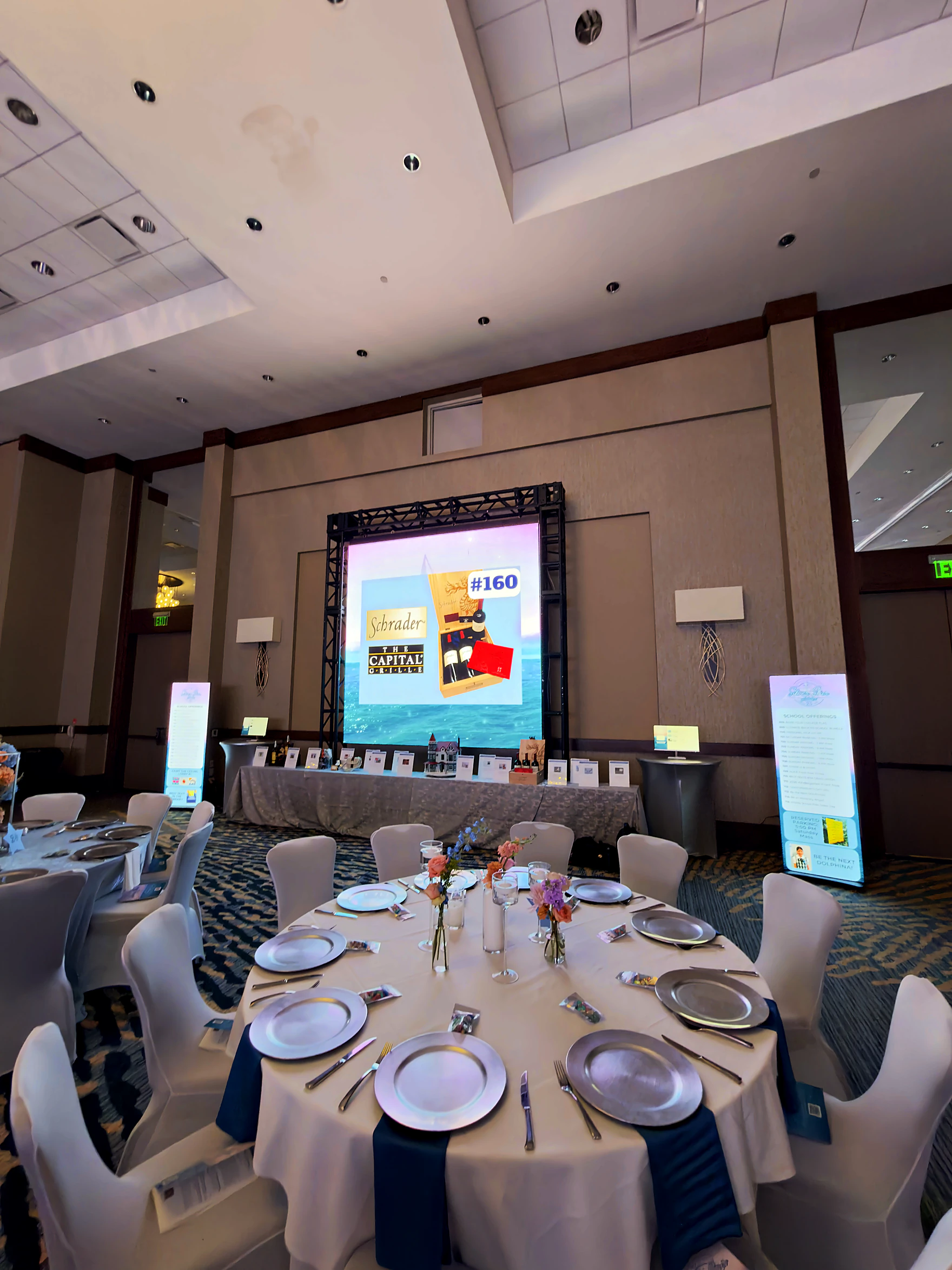 Auction lot on the big screen beside its staged display table and a set place setting