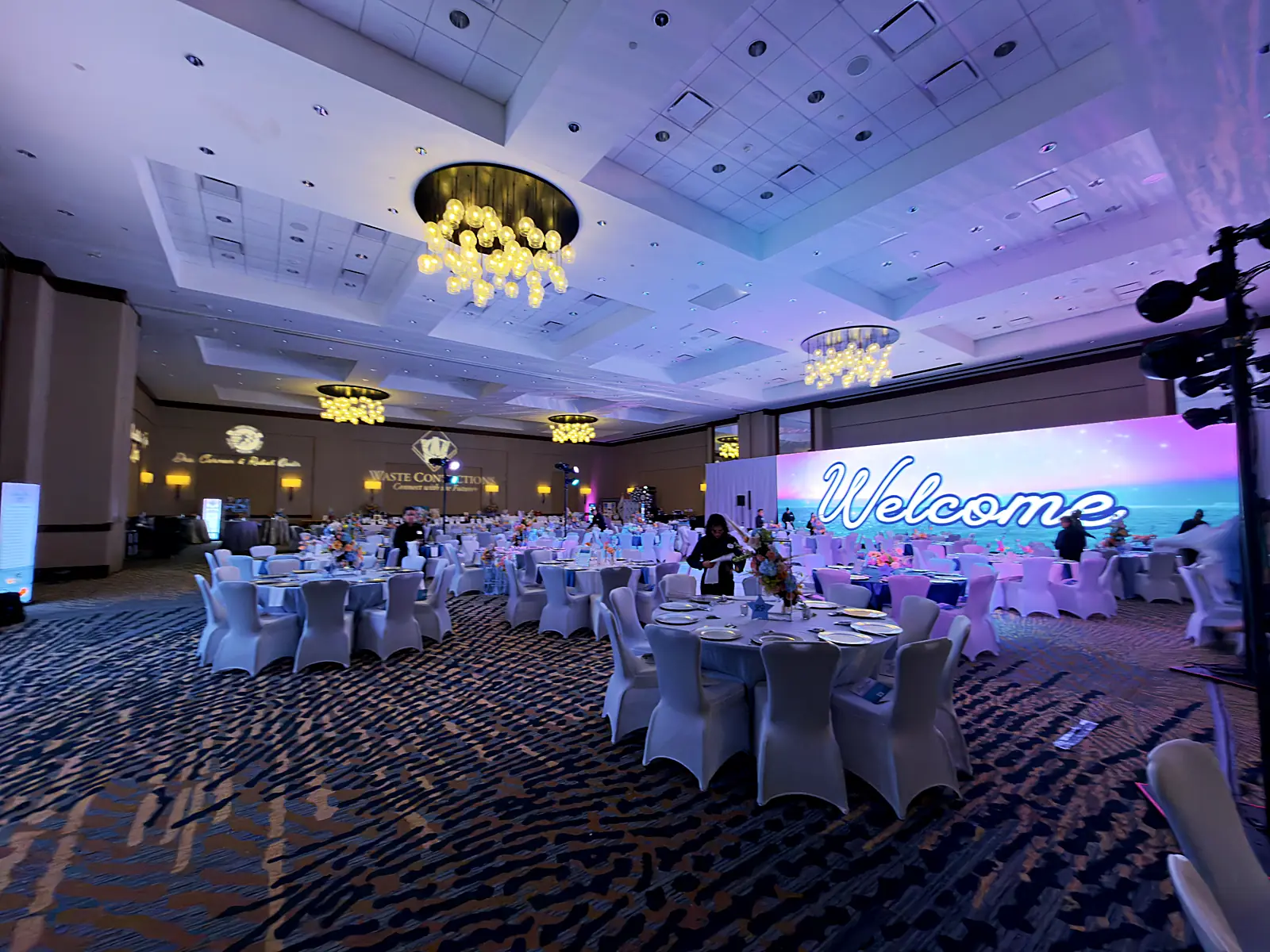 Gala ballroom set for the evening: Welcome LED wall over dressed rounds.