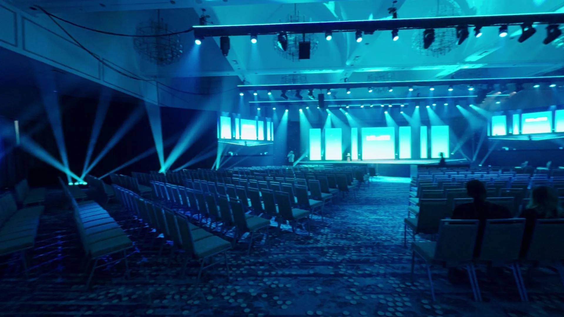 The finished general session in show state: teal wraparound LED and beam lighting across the ballroom